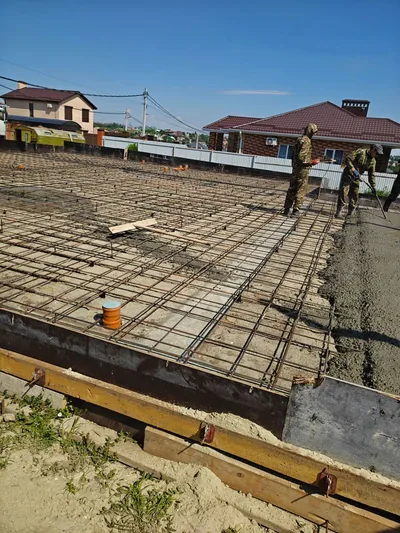 Арматурный каркас большой плиты в деревянной опалубке, двое рабочих у края